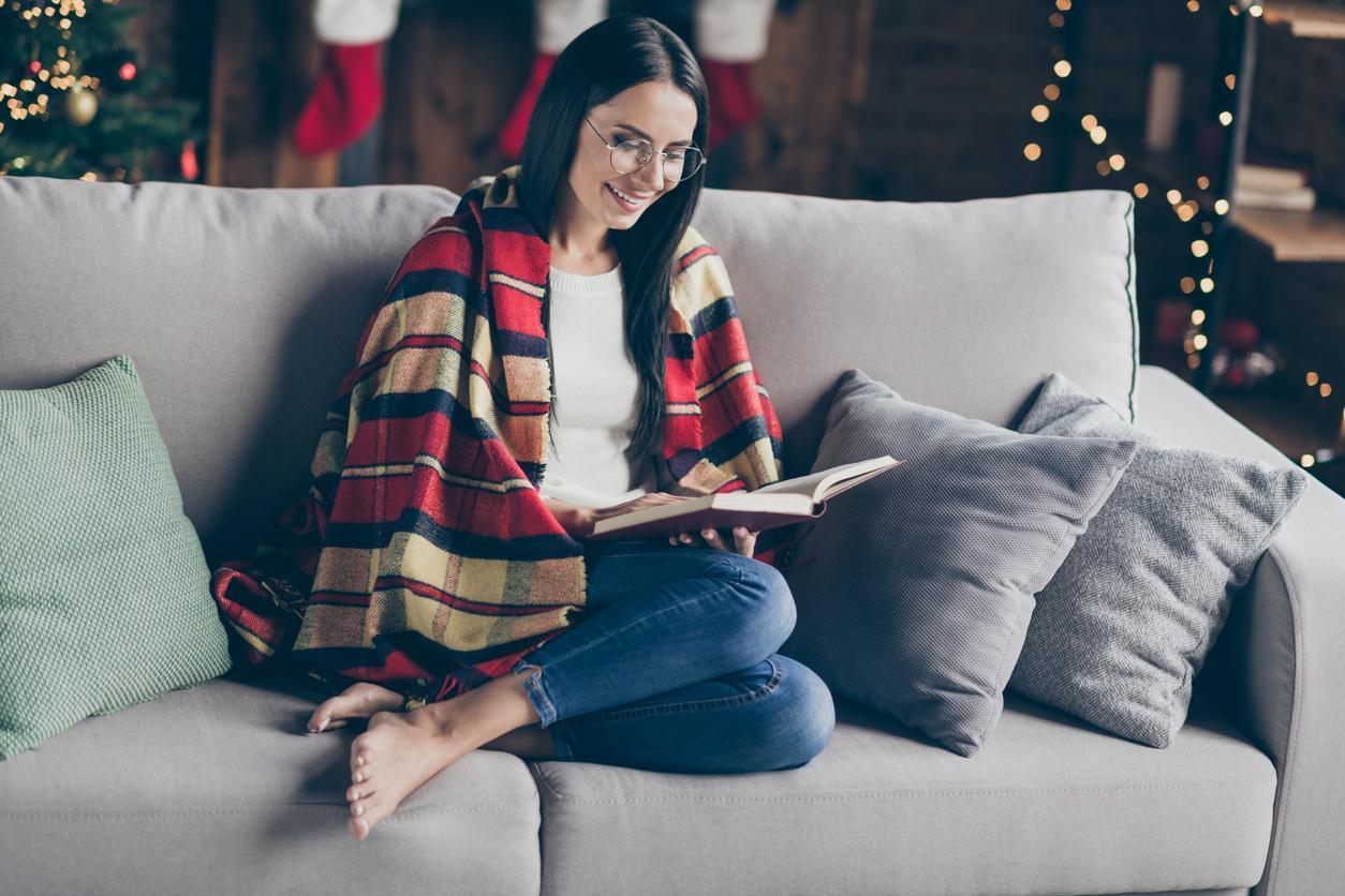 Žena na gauči čítajúca knihu a užívajúca si Vianočné sviatky
